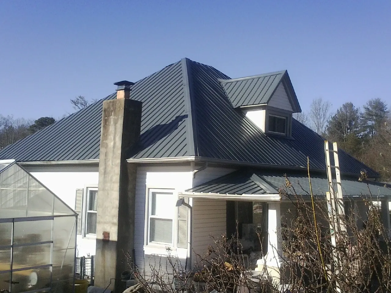 Dark blue standing seam metal roof on a white farmhouse with dormer — Slate & Tile Roof Repair by Roofing Brothers in Clinton